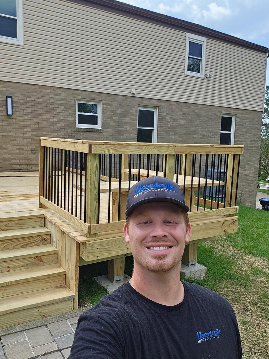 Chandler Usenicnik in front of a new wood deck with black balusters and stairs that his crew just built