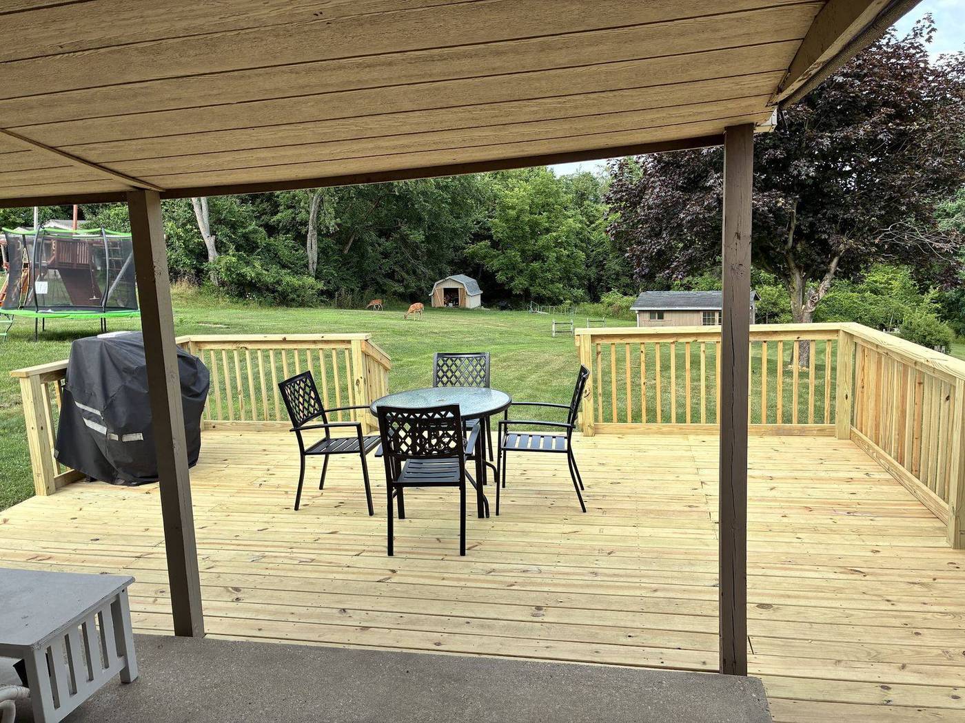 New pressure-treated wood deck with railings off a covered patio, table and chairs set out