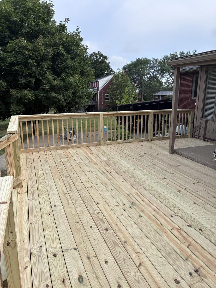 New wood deck with wood picket railing off the back of a brick home