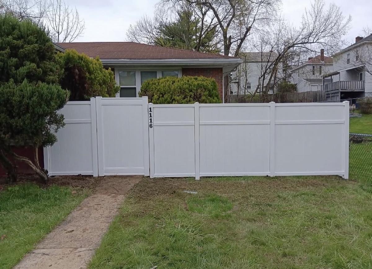 White vinyl privacy fence and gate across the side yard of a brick ranch home